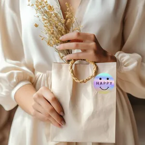 Close-up of a holographic laser smiley face sticker with HAPPY text on a beige gift bag
