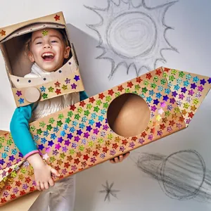 Child using colorful holographic star stickers on cardboard rocket and helmet