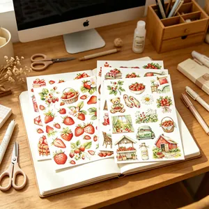 Hand-drawn watercolor strawberry sweetheart stickers displayed on an open notebook on a desk