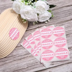 Detail view of pink round Fragile stickers with 'Handle with Love' text on wood