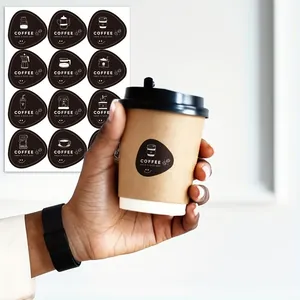 Hand holding a coffee cup decorated with a black sticker featuring coffee icons and text