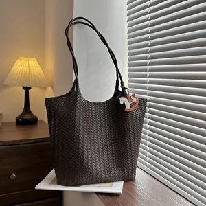 Vista dettagliata di una grande borsa tote intrecciata marrone su superficie in legno.