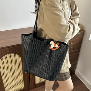 Dettaglio di una grande borsa tote nera intrecciata a mano con ciondolo a cavallo su modella.