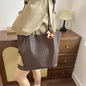 Dettaglio di una grande borsa tote intrecciata marrone indossata in una stanza calda