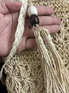 Close-up macro view of the handmade woven hollow-out pattern and tassel on cream straw bag