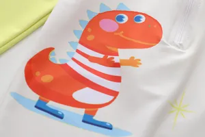 Close-up detail of the colorful cartoon dinosaur print on a white kids' swimsuit