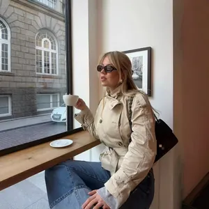 Elegante trench corto beige a doppiopetto con cintura mostrato in un ambiente cafe
