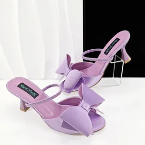 Élégants talons hauts en satin violet avec bout ouvert et un grand nœud décoratif.