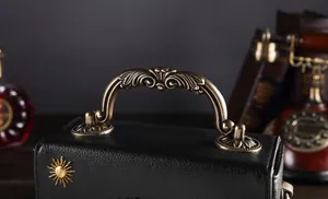 Detailansicht des antiken Bronzegriffs und des Sonnenornaments an einer schwarzen Vintage-Tasche.