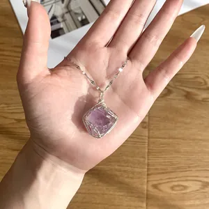Close-up of handmade wire wrapped amethyst raw stone pendant on a delicate chain.