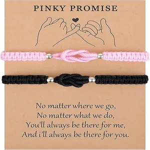 Close-up of pink and black braided pinky promise bracelets on a kraft gift card.