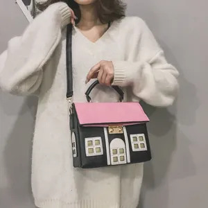 Creative house-shaped crossbody bag in pink and black worn by a model over a white sweater.