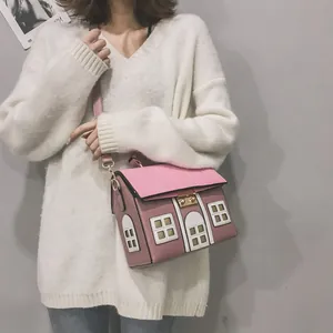 Detail shot of a pink house-shaped crossbody bag worn with a white sweater for a cute look.