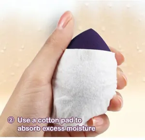 Close-up showing a hand using a cotton pad to blot excess water from a purple makeup sponge