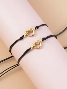Close-up of gold-plated stainless steel heart knot bracelets on black braided wax cord