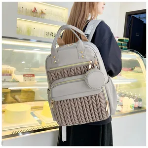 Modischer grauer Wickelrucksack mit Steppmuster, am Modell im hellen Café gezeigt.