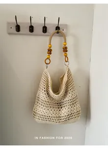 Handmade crochet beach hobo bag with wooden bead straps shown hanging on a white wall hook