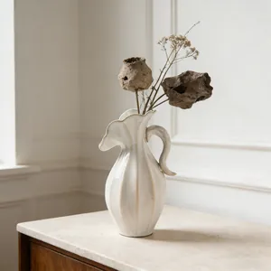 Detail van moderne crème keramische vaas met golvende textuur en elegant handvat voor bloemen.