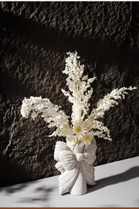 Detailed shot of white bow-shaped ceramic vase with textured surface and dried flowers.
