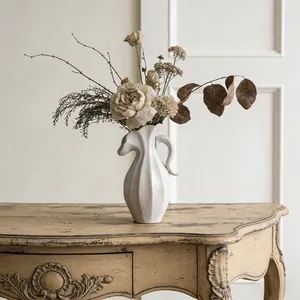 Elegante witte keramische kan vaas met droogbloemen op een vintage houten console