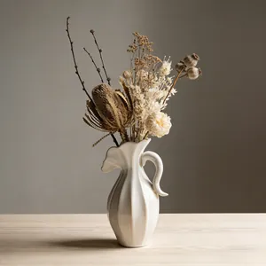 Elegante crèmekleurige keramische vaas met een droogbloemstuk op een houten tafel