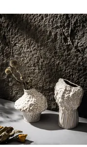 Artistic creamy white ceramic vase with organic cratered texture for home decoration.