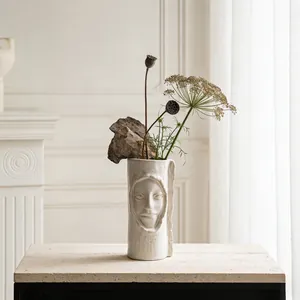 Artistieke witte keramische vaas met gezichtsreliëf en droogbloemen op een stenen sokkel