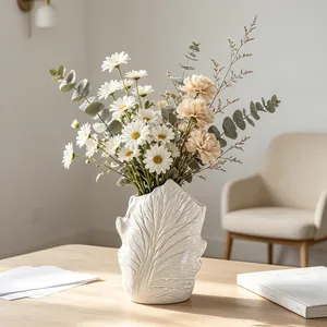 Close-up of white leaf-vein ceramic vase with daisies in a wabi-sabi home setting
