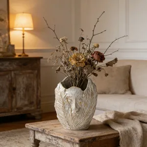 Detailed view of artistic face relief ceramic vase with dried flowers in a warm home setting.