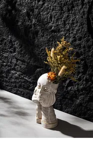 Artistic white ceramic human face vase with dried flowers in a textured stone setting