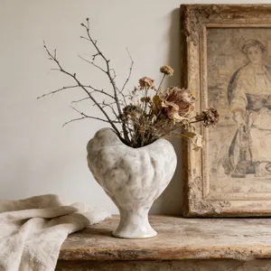 Artistic close-up of textured white ceramic vase with dried flowers in rustic setting