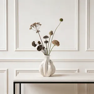 Detailed view of a minimalist white ceramic vase with organic wavy texture and dried flowers