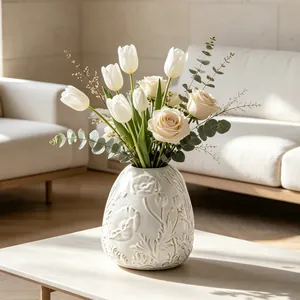 Detailed view of an elegant cream ceramic vase with floral relief on a coffee table.