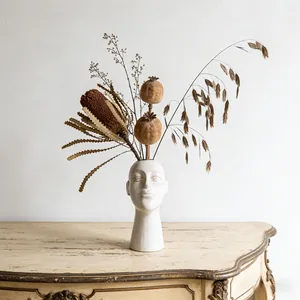 Artistic white ceramic human face vase with dried flowers on a vintage console table