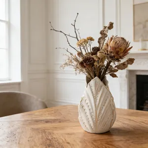 Dettaglio di vaso artistico in ceramica bianca con texture a foglia su tavolo in legno.