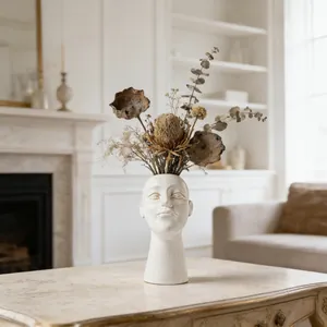 Artistic ceramic face-shaped vase featuring dried flower arrangements on a marble tabletop.