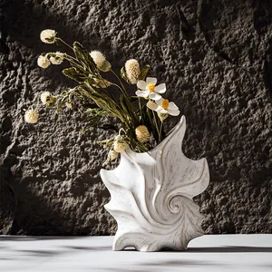 Vaso artistico in ceramica bianca a forma di conchiglia con fiori secchi su pietra