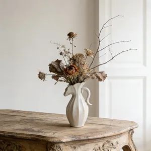 Elegante crèmekleurige keramische pitcher vaas met droogbloemen op een rustieke tafel