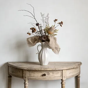 Moderne witte keramische vaas met handvat en droogbloemen op een vintage houten tafel