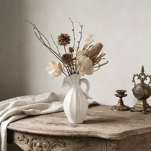 Detailweergave van een crème keramische vaas met droogbloemen op een antieke tafel