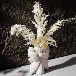 White ceramic bow-shaped vase with elegant dried flower arrangement in artistic lighting