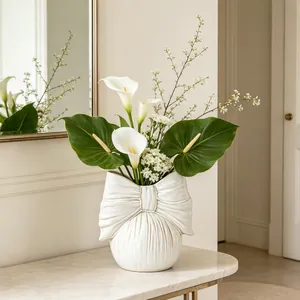 Detailed view of a minimalist white ceramic bow-shaped vase with elegant white calla lilies.