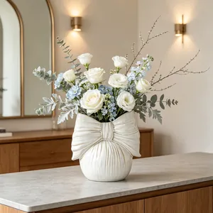 Detailed view of cream bow ceramic vase featuring fresh white roses and greenery decor