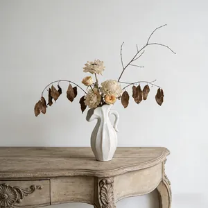 Elegante crèmekleurige keramische vaas met droogbloemen op vintage houten bureau