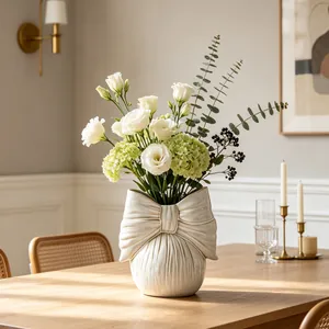 Elegant cream ceramic bow-shaped vase with fresh flowers on a wooden table setup