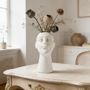 Artistic ceramic humanoid face vase holding dried flowers on an elegant vintage table.