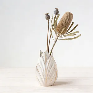 Dettaglio di un elegante vaso in ceramica bianca con texture a foglia e fiori secchi