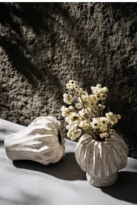 Close-up detail of textured white ceramic vases with dried flowers on a rustic stone wall