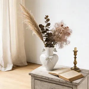 White heart-shaped ceramic vase with bow relief on a rustic wooden side table decor