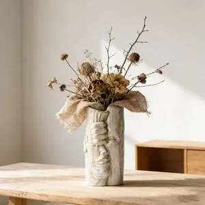 Vaso creativo in ceramica bianca con viso umano e fiori secchi su tavolo rustico
